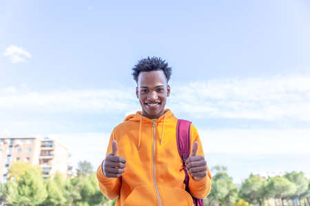 Handsome guy with afro hair and sweatshirt makes Ok with both hands with a clear sky in the...