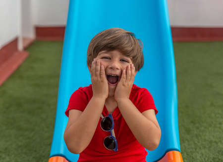 Happy child on a blue slide in the garden of a house on artificial grassの写真素材