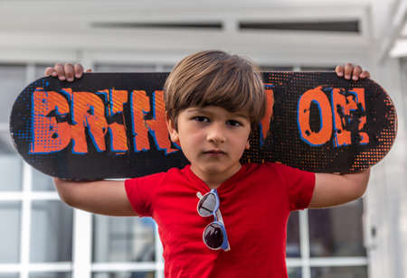Close-up of a handsome boy with his skateboard on his back in the backyard of his houseの写真素材