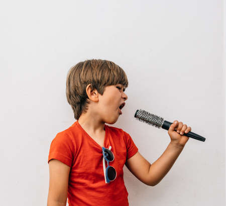 Caucasian blond boy in red t-shirt pretends to sing with a combの写真素材