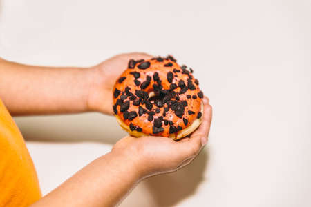 The hands of a boy hold a delicious orange donutの写真素材