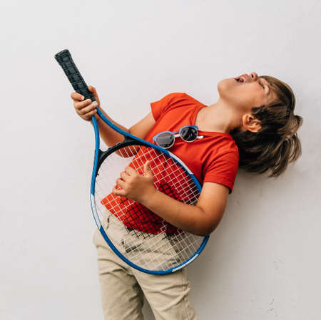 Very happy blond boy in t-shirt plays his racket as if it were a guitar