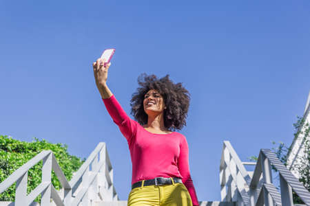 Beautiful and attractive afro-haired woman takes a photo of herself walking down some stairs
