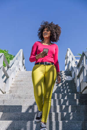 Dark skinned woman smiles walking down some stairs on a sunny summer dayの写真素材