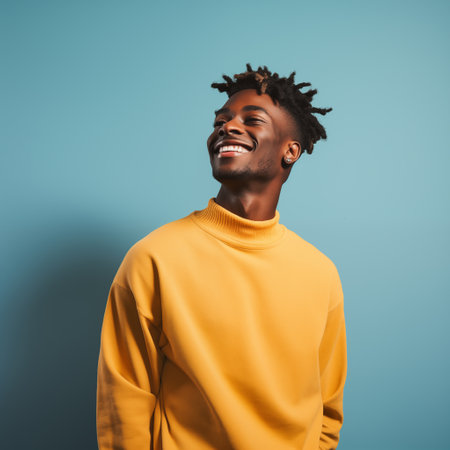Young African American man standing in yellow clothing, light blue background, with cheerful and optimistic expression.の素材