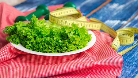 Fitness composition of green lettuce on white plate, weights and rulerの写真素材