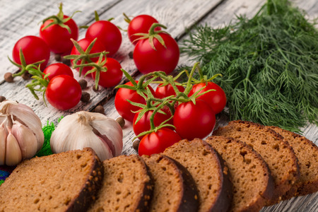 Still life on wooden background: tomatoes, black bread, garlic, fennel, bayberry pepperの写真素材