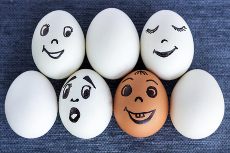 Seven funny eggs with drawn faces in two rows, one is red, another face is surprised, on grey backgroundの写真素材