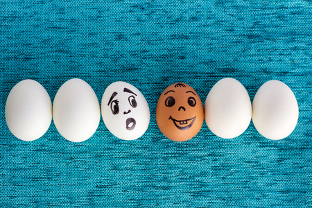 Funny eggs in row, one is red, another face is surprised, on blue backgroundの写真素材