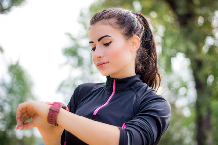 Young fitness girl checks stopwatch tracker on her wrist during running outdoorの写真素材