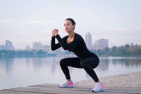 Young pretty fitness woman exercises on pier during morning training workoutの写真素材
