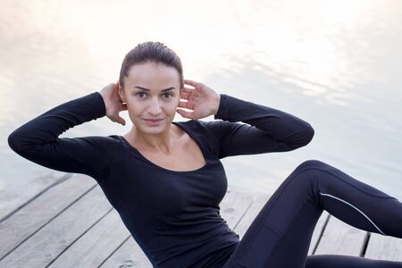Young pretty fitness woman exercises on pier during morning training workout