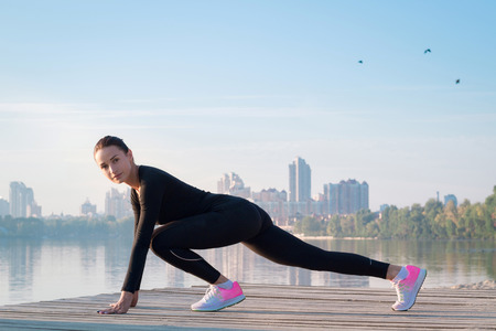 Young pretty fitness woman exercises on pier during morning sport training workoutの写真素材