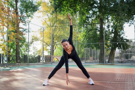 Young pretty fitness woman does stretching exercises during sport training workout on playground outdoorの写真素材