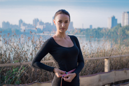 Young pretty fitness woman measures her waistline at morning river and city on backroundの写真素材