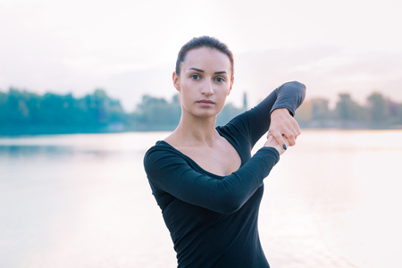 Young fitness woman stretches on pier during training exercises workout on early morning sunrise timeの写真素材