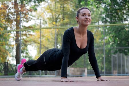Young pretty fitness woman does stretching exercises during sport training workout on playground outdoorの写真素材