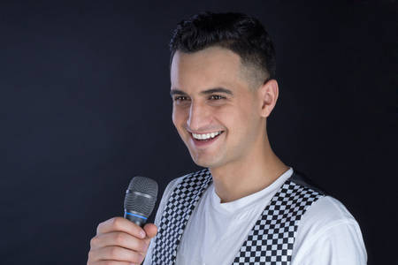 Young black-haired man dressed in black and white performs singing to microphoneの写真素材