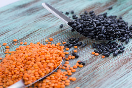 Batch of yellow lentils, black kidney beans scattered on metal spoons on wooden backgroundの写真素材