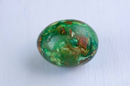 Multicolored green Easter holiday egg on white wooden natural backgroundの写真素材