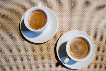 Composition of two cups of coffee on white serving plates with small metal spoonsの写真素材