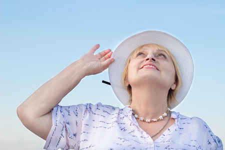 Happy smiling elderly retired lady woman watches sky holding her white hatの写真素材