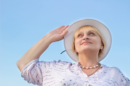 Happy smiling elderly retired lady woman watches sky holding her white hatの写真素材