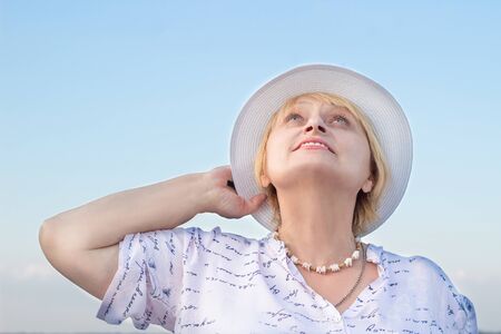 Happy smiling elderly retired lady woman watches sky holding her white hatの写真素材