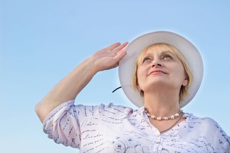 Happy smiling elderly retired lady woman watches sky holding her white hatの写真素材