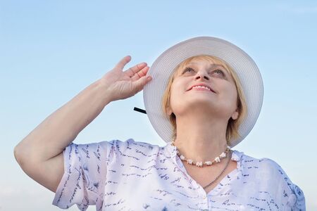 Happy smiling elderly retired lady woman watches sky holding her white hatの写真素材