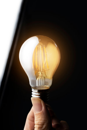 Hand holding a light bulb on a black background., Expression of ideas and intellectual creativityの写真素材
