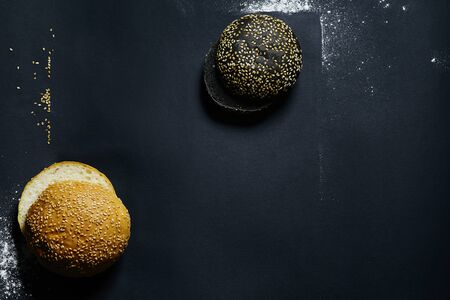 top view of two black and white burger rolls on a black background with sesame and flourの写真素材