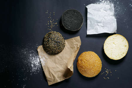 top view of two black and white burger rolls on a black background with sesame and flour
