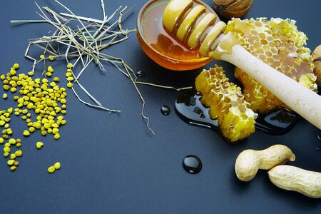 honey bee flows out of honeycomb on a black background, wooden spoon for honey and nutsの写真素材