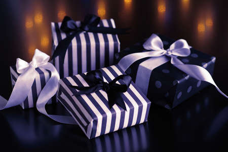 Gift boxes with bows for Christmas holidays on a dark background, with a reflection of colored...