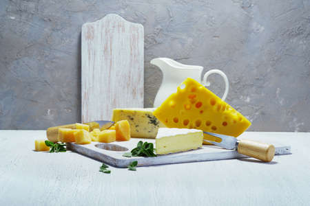 Different kinds of cheeses and a jug of milk on a white old board. Rustic view. Light background.