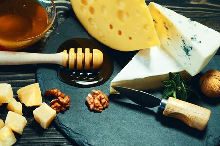 Varieties of cheeses with honey and nuts on a dark wooden table.の写真素材