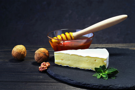 A piece of brie cheese with honey and nuts on a dark wooden table.の写真素材