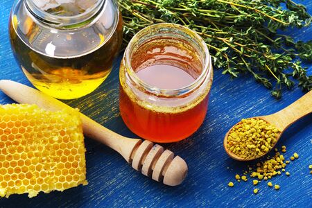 Transparent honey in glass jars with honeycomb and herbs on a bright blue old board.