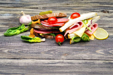 Fresh appetizing sandwiches with salami, vegetables, ham and cheese on a wooden table.の写真素材