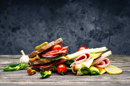 Fresh appetizing sandwiches with salami, vegetables, ham and cheese on a wooden table.の写真素材