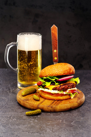 Delicious beef burger with a glass of beer on the board with cheese, vegetables and lettuce, hand made, according to a classic recipe .の写真素材