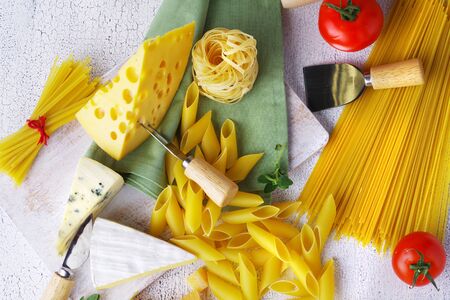 Close-up of raw pasta and a variety of cheeses scattered on a light rustic table.の写真素材