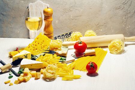 Varied types of pasta and cheeses, tomatoes and ingredients for cooking on a light rustic...
