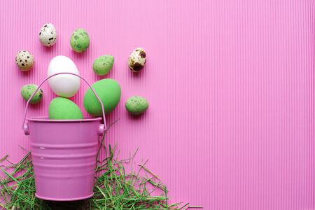 Easter eggs in a decorative pink bucket with green grass on a pink background. Top view. Space for text. Punchy pastels.の写真素材