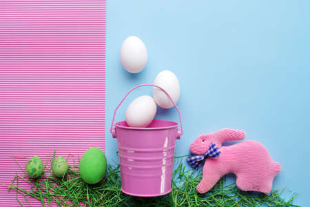 Easter eggs and handmade rabbits with  decorative pink bucket on a pastel blue-pink background. Easter concept. Top view. Punchy pastelsの写真素材