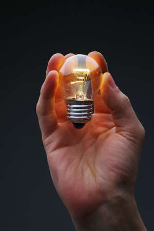 A man's hand holds a glowing light bulb on a dark background.の写真素材