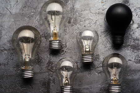 A few burned old bulbs and one black light bulb on a gray concrete background. Top view.の写真素材