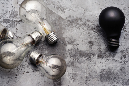 A few burned old bulbs and one black light bulb on a gray concrete background.