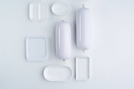 White food product in the form of sausage and white tableware on a white background. Top view. Flat...